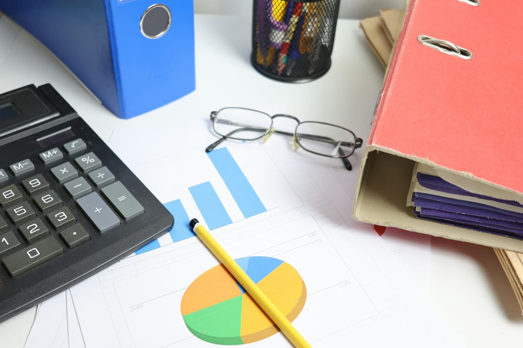 A tidy desk with a calculator, glasses, folders and printed charts