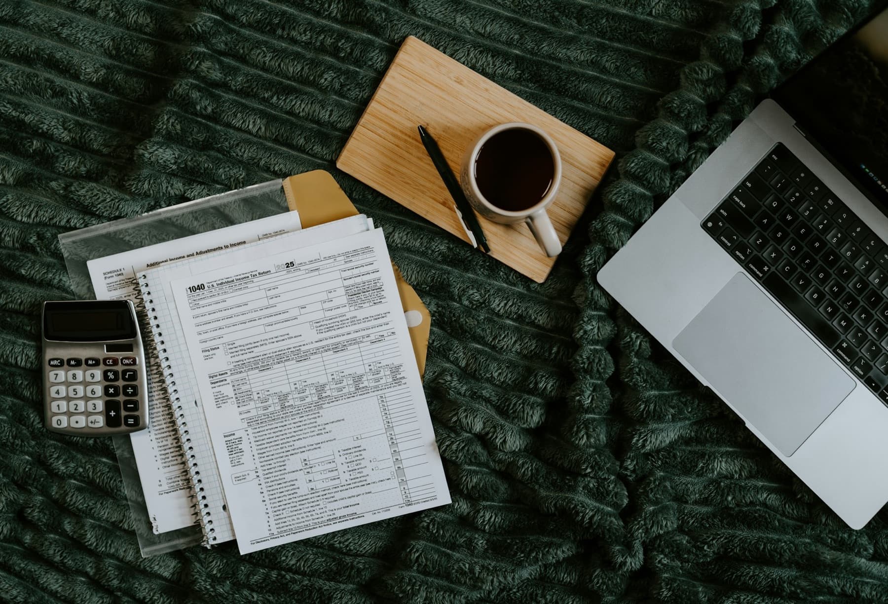 A flat lay of forms, a calculator, coffee and a laptop