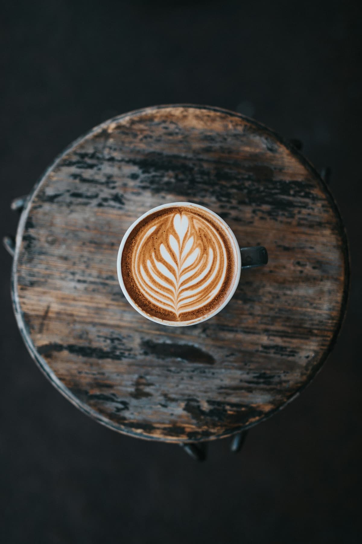 Cup of coffee with leaf latte art on a wooden stool