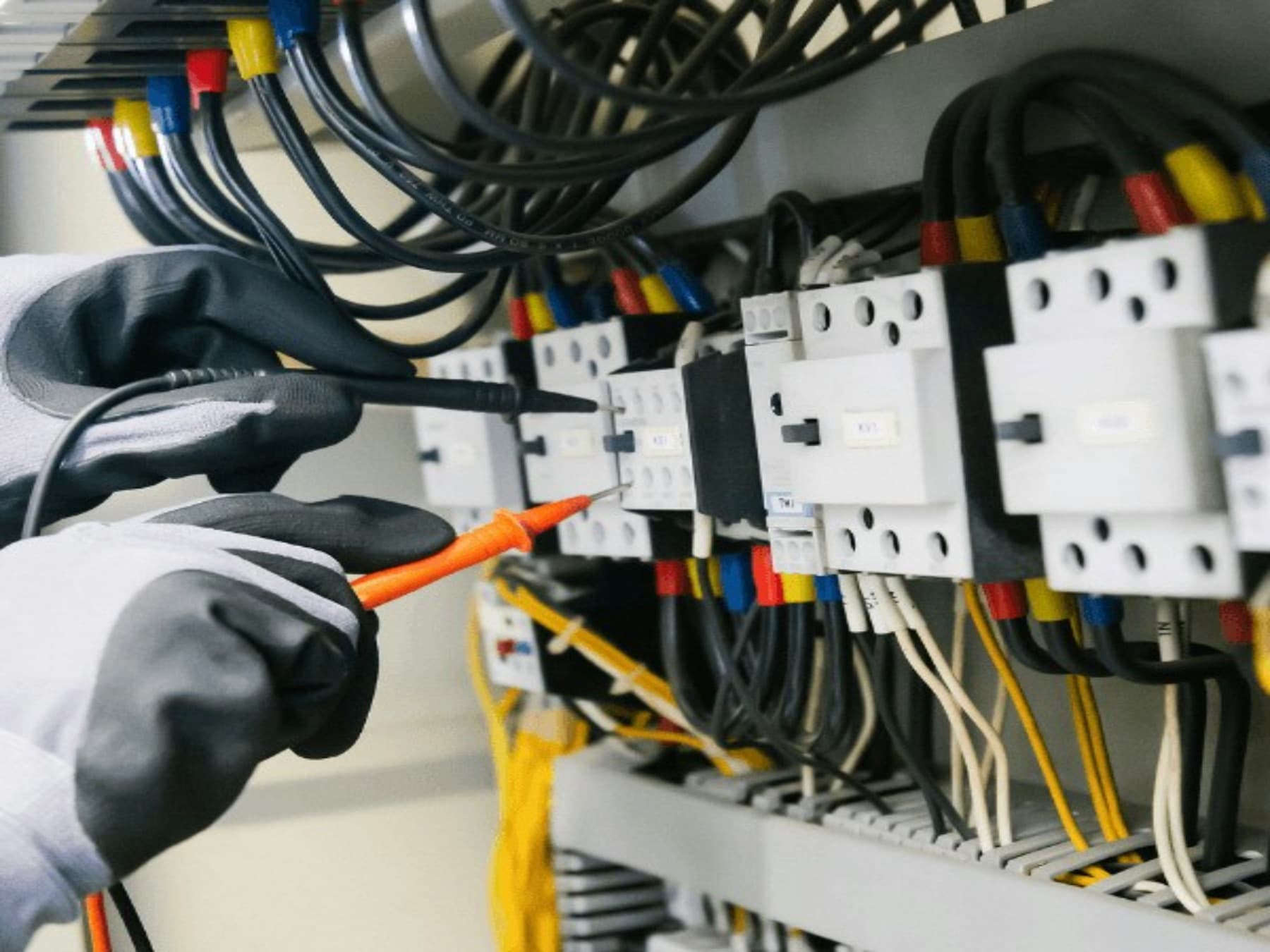 Gloved hands testing a switchboard with a multimeter probe